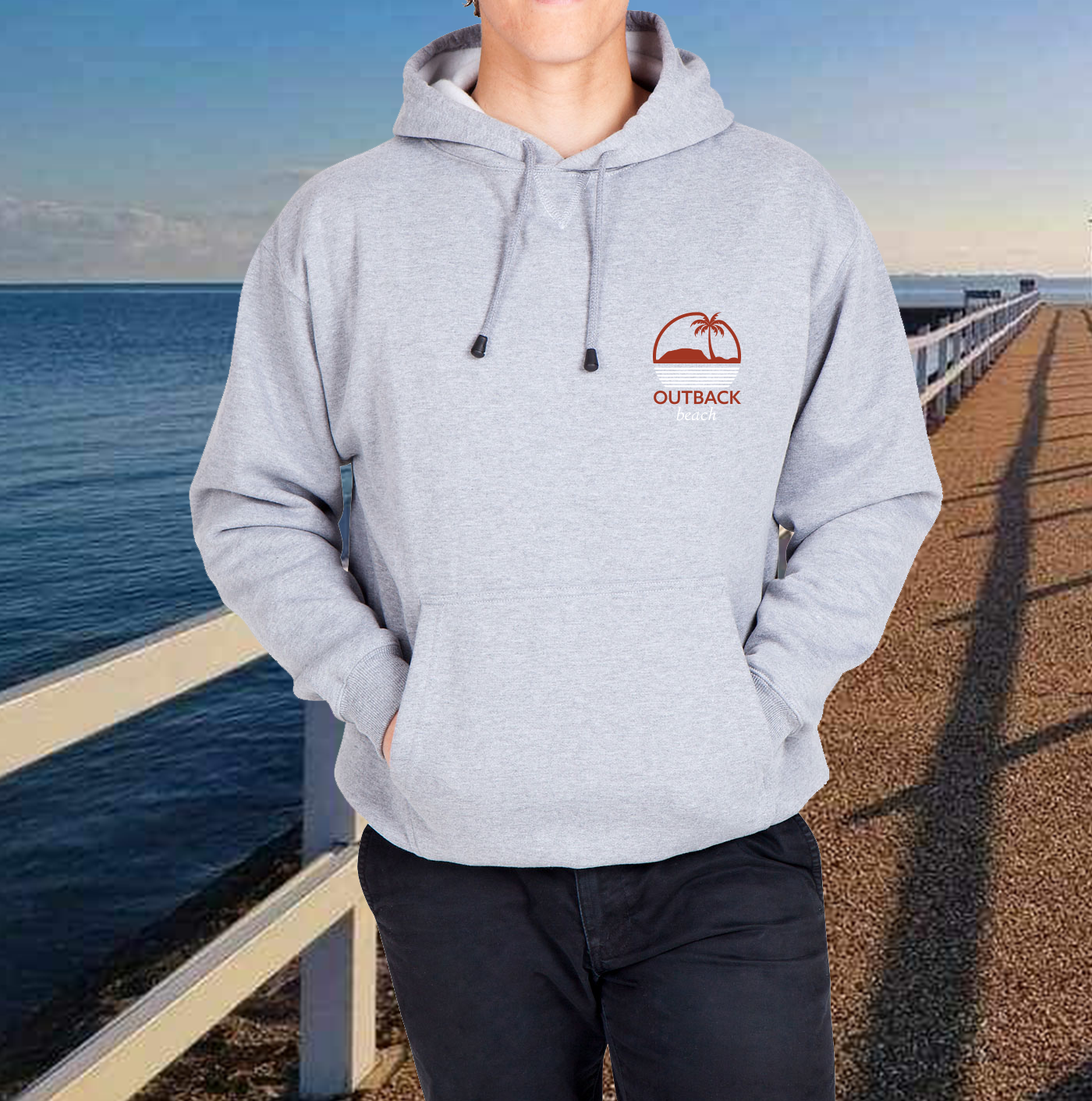 A person wearing a gray Kangaroo Hoodie with the brand 'OUTBACK' visible on the logo, standing by the sea.